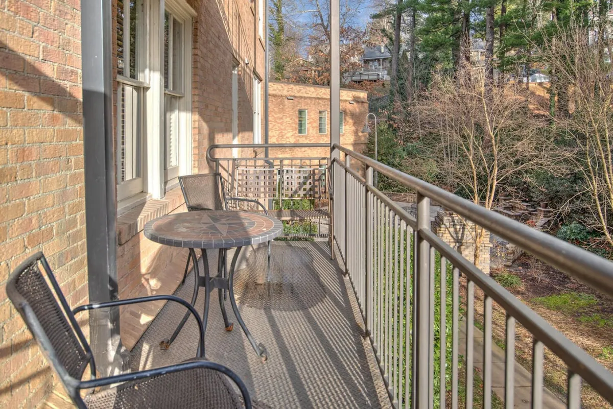 A peaceful balcony scene with a round table and two chairs overlooks verdant greenery. The balcony’s railing frames the view, suggesting a perfect spot for quiet moments, sunrises, or evening gatherings, and evokes the sense of being nestled in a scenic environment.