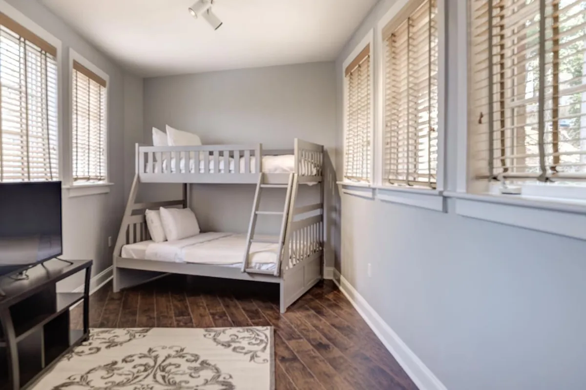 A family-friendly bonus room featuring a twin-over-full bunk bed, a television, a soft rug, and windows that infuse the space with light. The playful yet comfortable setup makes it ideal for children or extra guests.