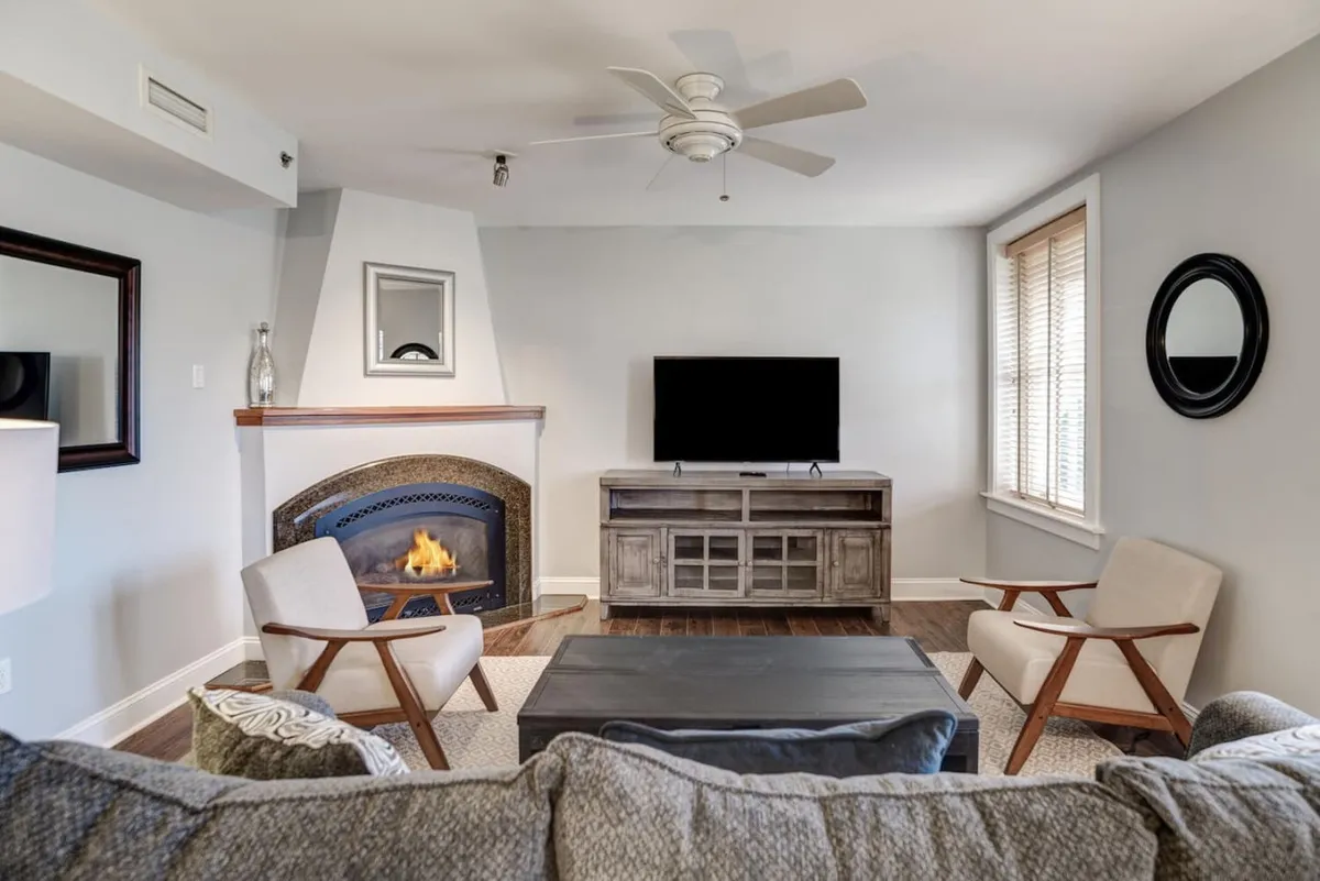 This image features a cozy living area with a fireplace, a TV unit, and a comfortable seating arrangement. The ample seating, soft lighting, and inviting atmosphere make it a natural spot for gatherings and relaxation. The renovated touches are visible in the finishes and styling, while the historic character is preserved in the architectural details.