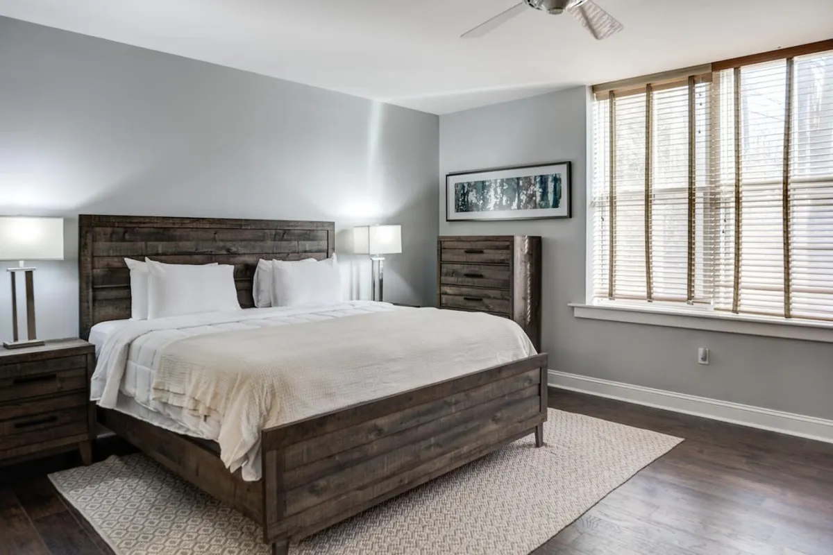 A tranquil bedroom with a plush bed, nightstands, window, and tasteful artwork. Sunlight gently filters in, creating a serene, inviting atmosphere ideal for unwinding together.