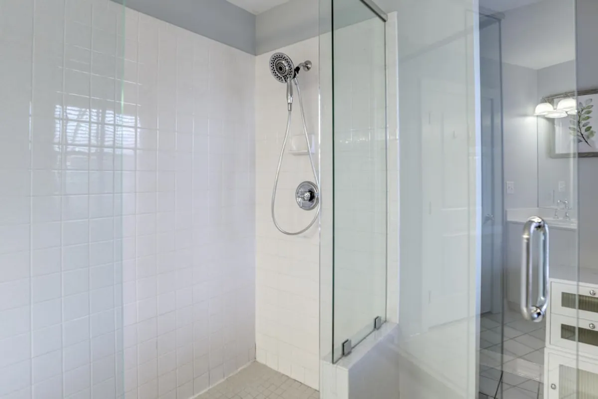 A close-up of a luxurious glass shower enclosure with sleek tiled walls and a rainfall-style shower head. The space gives a sense of indulgence and relaxation, offering a modern take on classic comfort.