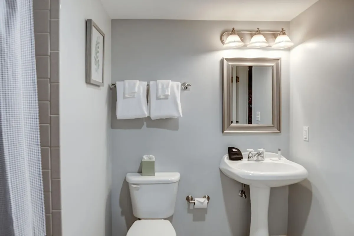 A stylish bathroom with a large mirror, elegant sink, fresh towels, and neutral color palette. The space feels tranquil and thoughtfully designed, with subtle nods to historic charm through its materials and layout.