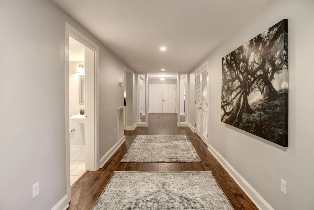 A calm and inviting hallway lined with artwork and runner rugs, with several closed doors leading to different rooms. The space feels open and welcoming, suggesting easy movement between areas and glimpses of home life.