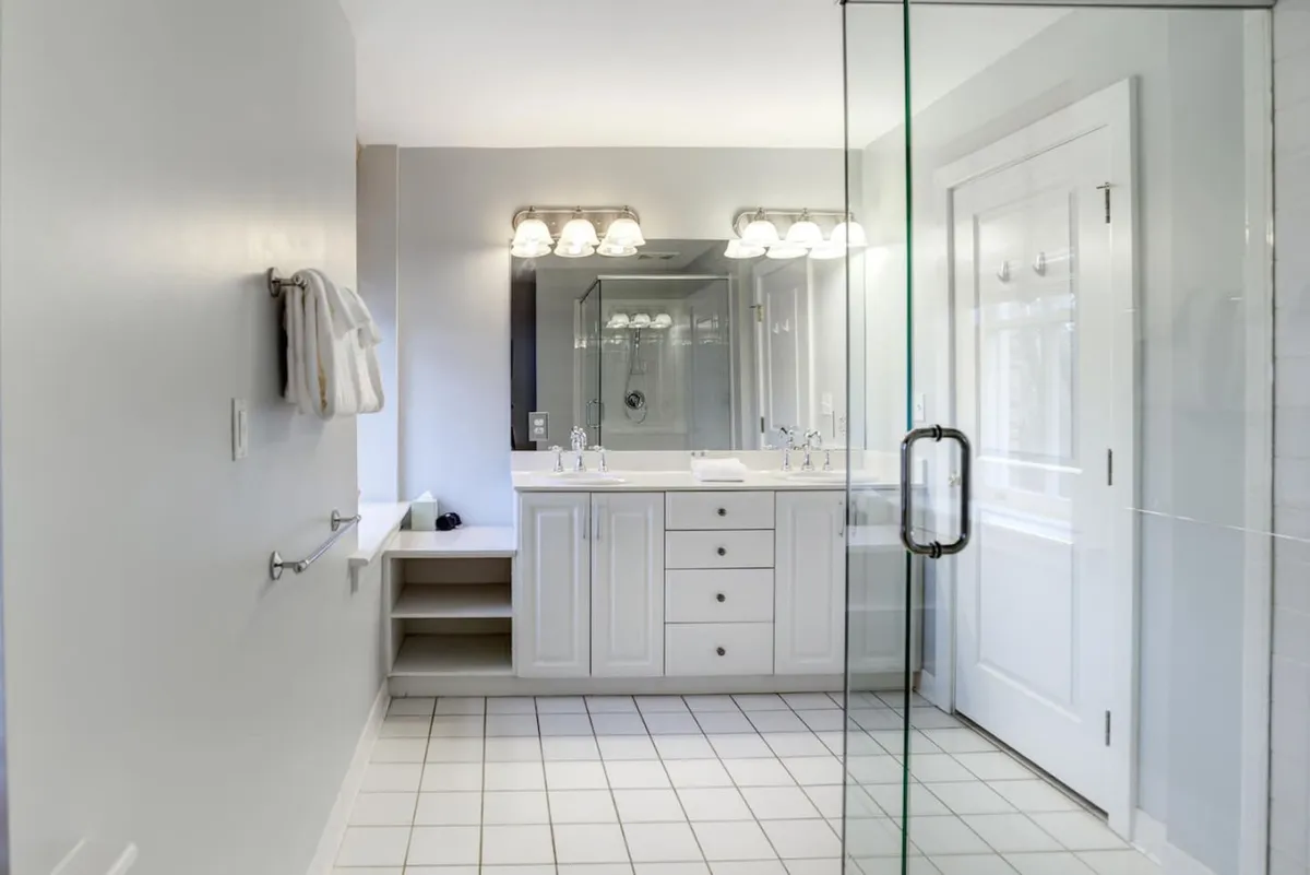 A bright and modern bathroom featuring a spacious vanity with double sinks, a wide mirror, and a glass-enclosed shower. The space is fresh and inviting, with contemporary fixtures that emphasize comfort and style.