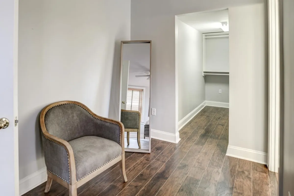 This image features a calm and stylish corridor with an inviting armchair, a full-length mirror, and an open hallway leading toward the rest of the condo. The scene suggests a transition space, ideal for preparing to step out into Asheville or relaxing after a day of exploration.